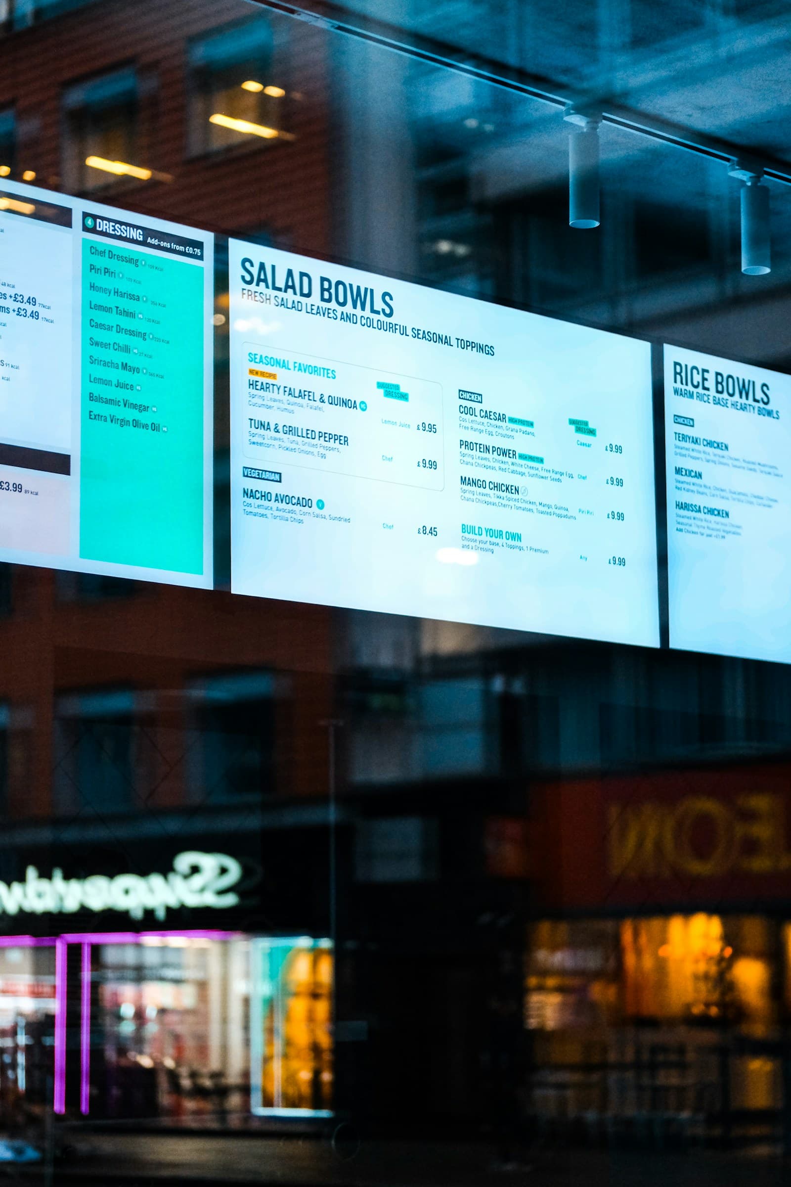 Digital menu boards in a restaurant window showing salad and rice bowls